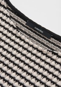 Black and beige knitted fabric with horizontal stripes and a black clothing label reading "someday." near the top edge.