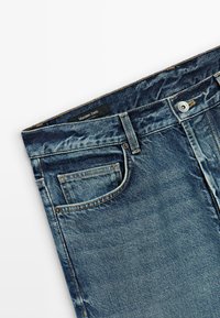 Jeans in denim blu scuro presentano un classico design a cinque tasche, una chiusura con bottone metallico e una leggera usura su tutta la superficie. Etichetta visibile all'interno.