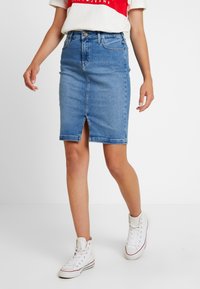 Lichtblauwe denim kokerrok met een voorlitzak, aansluitend ontwerp en vijf-pocket stijl, gecombineerd met witte high-top sneakers.