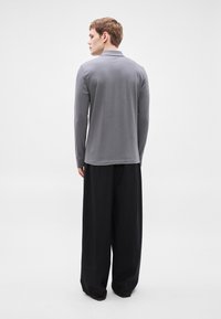 Langärmliges, graues Poloshirt aus weichem Stoff, mit Kragen und geradem Schnitt. Kombiniert mit weiten schwarzen Hosen.