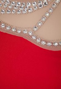 Robe rouge avec un haut en maille beige orné de cristaux le long du décolleté, créant un motif texturé contrasté.