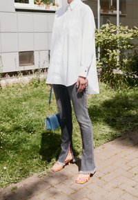 White oversized button-down shirt, gray flared jeans with side slits, orange sandals, and a small blue crossbody bag.