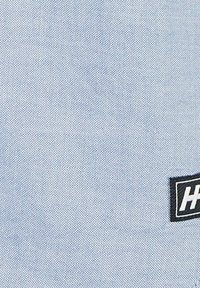 Blauwe stof met een fijne, gestructureerde weving en een zwart label waarop de letters "H" en "H" aan de rechter benedenhoek staan.