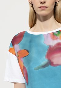 Kurzärmeliges T-Shirt mit blauer Basis, das mit floralen Mustern in Pink, Orange und Grün verziert ist, ergänzt durch einen weißen gerippten Ausschnitt.