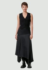 Colete preto acanalhado com botões combinado com uma saia preta fluida. O conjunto apresenta uma bainha assimétrica e botas pretas até ao joelho.