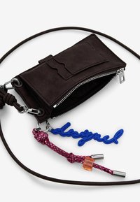 Portafoglio in suede marrone con chiusura a zip, hardware argentato e un portachiavi in gomma blu. Presenta un cordoncino intrecciato rosa e rosso e un accento trasparente.