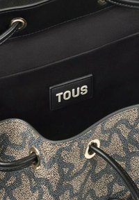 Bolso tipo bucket con un exterior estampado en beige y navy, que cuenta con asas de cuerda negras y una etiqueta de logo plateada en el interior.