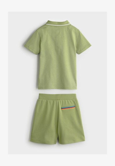 Zaļa kokvilnas divdaļīga kostīme, kas ietver īsām piedurknēm polo kreklu ar baltu apkakli un atbilstošas šortus ar svītraina kabatas akcentu.