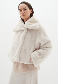 Faux fur-jacka i gräddvit med en bred krage, oversized passform och plyschig textur. Har slappa ärmar och ett mjukt underlager i rosé.