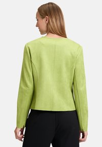 Zielona kurtka z sztucznego zamszu o dopasowanym kroju, z detalami szwu na plecach i długimi rękawami, w połączeniu z czarnymi spodniami.