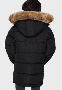 Doudoune noire avec capuche et col en fausse fourrure. Présente un design matelassé et une coupe décontractée. Le matériau semble lisse et isolé.