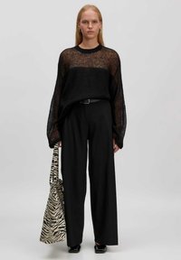 Zwarte doorschijnende gebreide trui met oversized mouwen, gecombineerd met brede zwarte broek. Accessoires omvatten een tas met zebra-patroon.