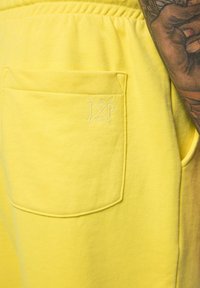 Joggers en coton jaunes avec une poche arrière dotée d'un logo brodé. Le tissu a une texture lisse et une taille élastique.