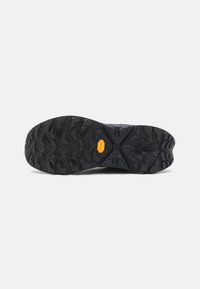 Fekete futócipő talp mély bordázattal és egy kiemelkedő sárga Vibram logóval. Texturált gumi a tapadás és tartósság érdekében.
