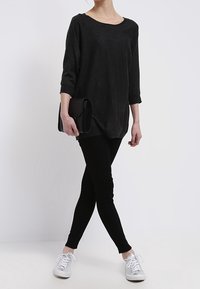 Maglietta nera ampia con maniche a tre quarti, abbinata a leggings neri e sneakers bianche. La maglietta ha un collo rotondo e una texture morbida.
