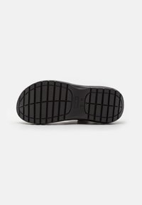 Semelle de chaussure noire en caoutchouc avec un motif texturé de rainures et de crêtes pour l'adhérence. Présente des bords arrondis et un design plat.