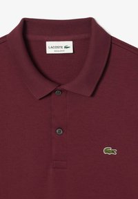 Burgundska polo majica z rebrastim ovratnikom, dvema črnima gumboma in zelenim krokodiljim logotipom na levem prsnem delu. Narejena iz mehke tkanine.
