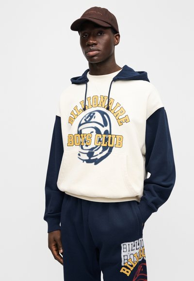 Κρεμ και ναυτικό φούτερ με κουκούλα, τύπωμα "Billionaire Boys Club", με μεγάλο γραφικό κράνος. Συνδυασμένο με αντίστοιχο ναυτικό παντελόνι φόρμας.