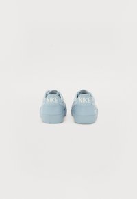 Heledad sinised Nike tossud, millel on sile tekstuur, ümar kuju ja valge logo aktsent kandadel. Mugavuseks mõeldud kummist välistald.