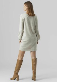 Abito maglione grigio chiaro in maglia, con maniche lunghe, vestibilità comoda e orlo a costine; abbinato a stivali in pelle beige al ginocchio.