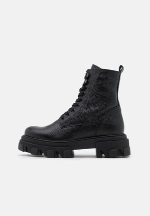 Botte de combat en cuir noir texturé avec semelle épaisse à crampons et laçage à l'avant, hauteur cheville avec languette à l'arrière.