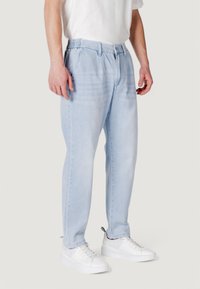 Pantaloni jogger in denim azzurro chiaro con vita elastica, vestibilità affusolata, tasche laterali e dettagli di sfumatura leggera. Indossati con sneaker bianche.