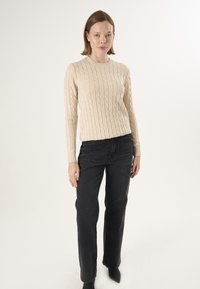 Hellbeige Strickpullover mit rundem Halsausschnitt, kombiniert mit hoch geschnittenen schwarzen Jeans und spitzen schwarzen Ankle Boots.