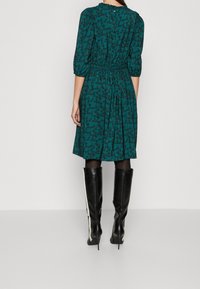 Turkoosi mekko, jossa on kukkakuosi, vyötäisiltä kiristetty ja kyynärpään mittaiset hihat, yhdistetty mustiin polvimittaisiin saappaisiin, joissa on valkoiset sivuraitat.