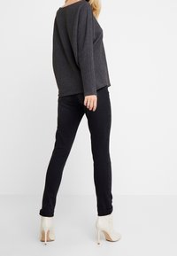 Szaroszary, oversize dziany sweter z długimi rękawami, połączony z czarnymi, obcisłymi jeansami oraz kremowymi, botkami na wysokim obcasie. Prosty design, casualowy wygląd.