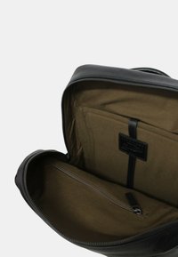 Borsa in pelle nera con un ampio interno foderato in tessuto marrone, una tasca con zip e un ulteriore scomparto con una tracolla.