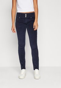 Pantaloni skinny in corduroy blu navy con chiusura a tre bottoni, due tasche frontali e tessuto texturizzato. Abbinati a sneaker bianche.