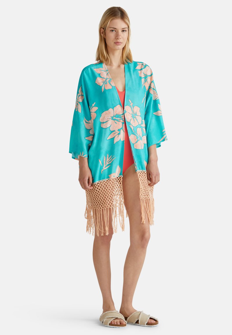 Tyrkysový kimono s růžovými květinovými vzory, zdobené háčkovaným třásněním na spodním lemu, přehodnoceno přes jasně korálové plavky.