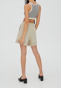 Shorts beiges avec ourlets retroussés, ceinture élastique, poches latérales. Associés à un crop top noir et blanc à rayures, mettant en valeur une coupe ajustée. Mules noires à talons.