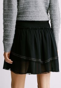 Gonna nera a strati con orlo trasparente, adornata con dettagli in metallo. Vita elasticizzata e tessuto leggero e fluido. Maglione grigio testurizzato sopra.