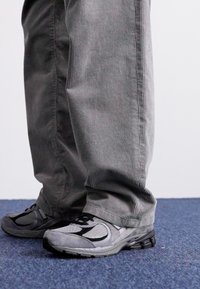 Calças de veludo cotelê cinza com riscas verticais, combinadas com sapatos de treino em preto e cinza com detalhes em malha e borracha.