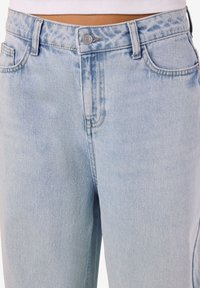 Šviesiai mėlynos spalvos džinsai iš denimo su šiek tiek blukintu paviršiumi. Turi sagos užsegimą, diržo kilpas ir penkių kišenių dizainą. Klasikinės tiesios kelnės.