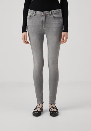 Jeans ajustados de mezclilla en un gris claro, con un ligero desgaste, diseño de cinco bolsillos y un botón de cobre sutil. Combinados con bailarinas negras.