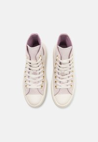 Para wysokich sportowych butów z płótna w jasnoróżowym kolorze z białymi sznurówkami, białymi gumowymi czubkami i złotymi oczkami na białym tle.