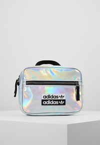 Bolsa Adidas holográfica de forma rectangular, con cierre de cremallera negro y dos parches de logo en negro en la parte frontal. Textura suave y brillante.