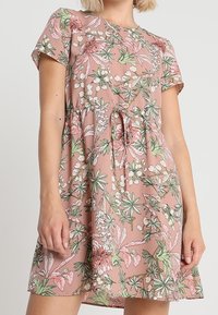 Vestido de manga corta floral en rosa con patrones botánicos en verde y blanco. Cuenta con una cintura con cordón y una tela suave y ligera.