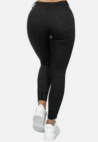 Black denim leggings with a fitted design, five pockets, frayed hem detailing, and paired with white sneakers.