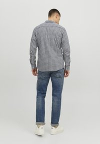 Camisa de cuadros en blanco y negro, con mangas largas, cuello abotonado y dobladillo curvado. Combinada con jeans de mezclilla azul y zapatillas blancas.