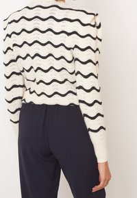 Pull blanc en maille avec un motif ondulé noir, doté d'un col arrondi et de poignets côtelés. Vue de dos montrant un design court et une texture.