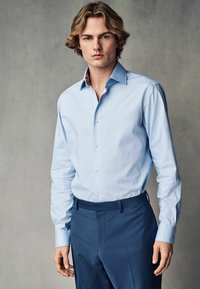 Cămașă cu mânecă lungă, de culoare albastru deschis, cu guler tip buton și guler interior cu un model contrastant, combinată cu pantaloni eleganți de culoare albastru închis.