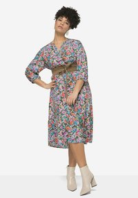 Robe portefeuille florale aux couleurs vives, manches trois-quarts, ceinture à la taille et jupe évasée. Associée à des bottes chelsea crème.