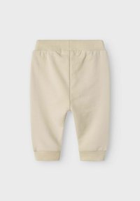 Ljust beige bomullsbyxor med elastisk midja, ribbade muddar och slät textur. Har en enkel, ren design.