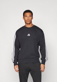 Sweatshirt preto com detalhes em branco de três riscas nas mangas, gola redonda e pequeno logo branco no peito. Feito de tecido macio.