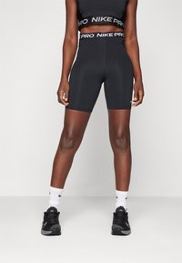 Black Nike Pro crop top and high-waisted shorts. Smooth, stretchy fabric with logo bands at the waist and a fitted design. Black sneakers and white socks.