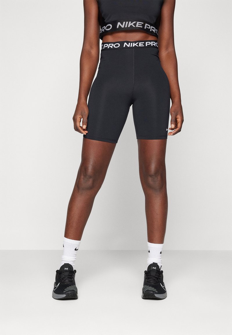 Black Nike Pro crop top and high-waisted shorts. Smooth, stretchy fabric with logo bands at the waist and a fitted design. Black sneakers and white socks.
