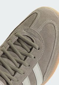 Γκρι δερμάτινο αθλητικό παπούτσι από σουέτ με λευκές ρίγες, στρογγυλή μύτη, υφασμένο επάνω μέρος και αντιθετική σόλα σε χρώμα καραμέλας. Λεπτομερής ραφή κατά μήκος των ραφών.